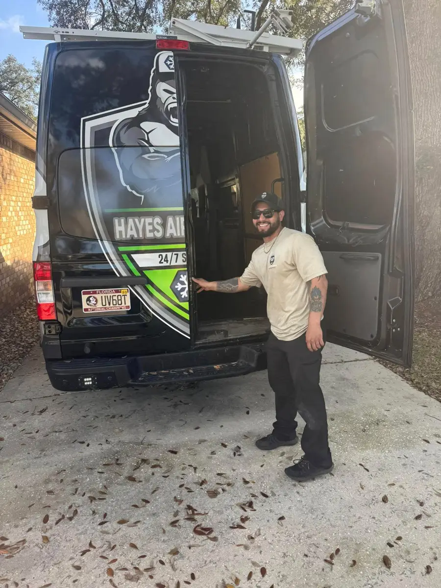 A man in sunglasses and cap smiling by open Hayes Air service van with branded rear doors