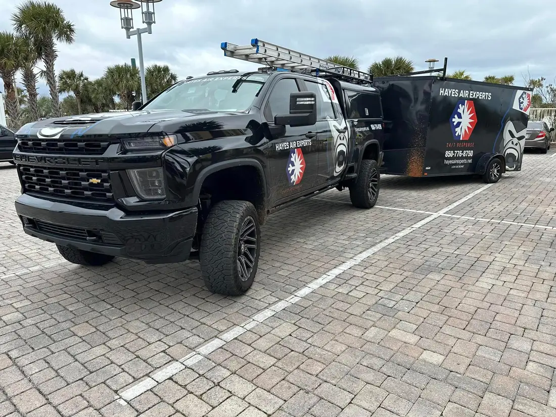 Black Hayes Air Experts service pickup with ladder and matching trailer parked on paved lot near palm trees
