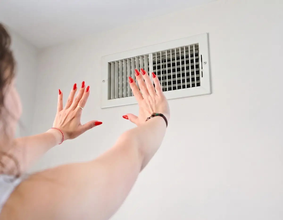 Woman with red nail polish reaching toward ceiling HVAC vent register