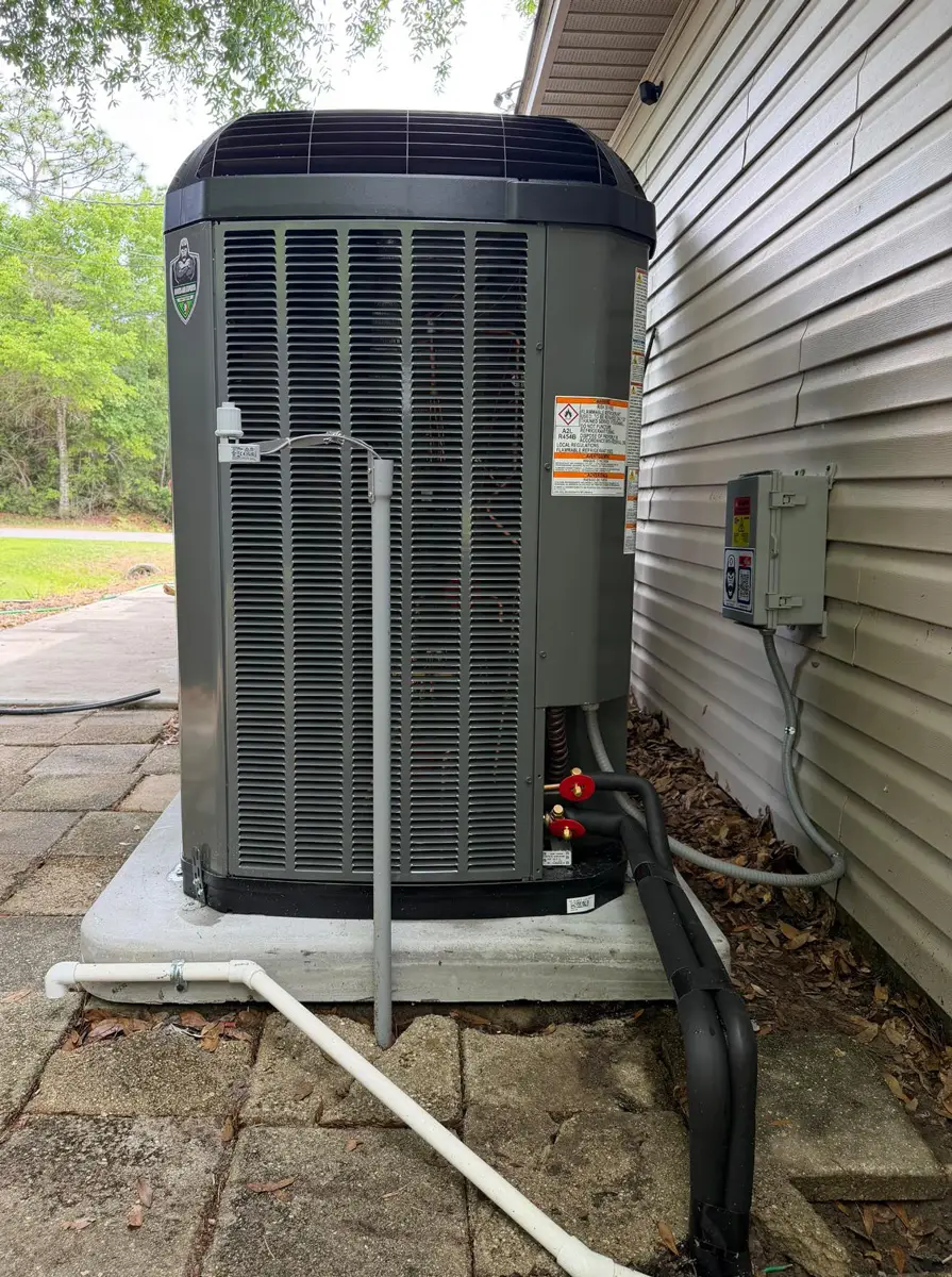 Outdoor air conditioner condenser on concrete pad beside house, insulated refrigerant lines and electrical disconnect.