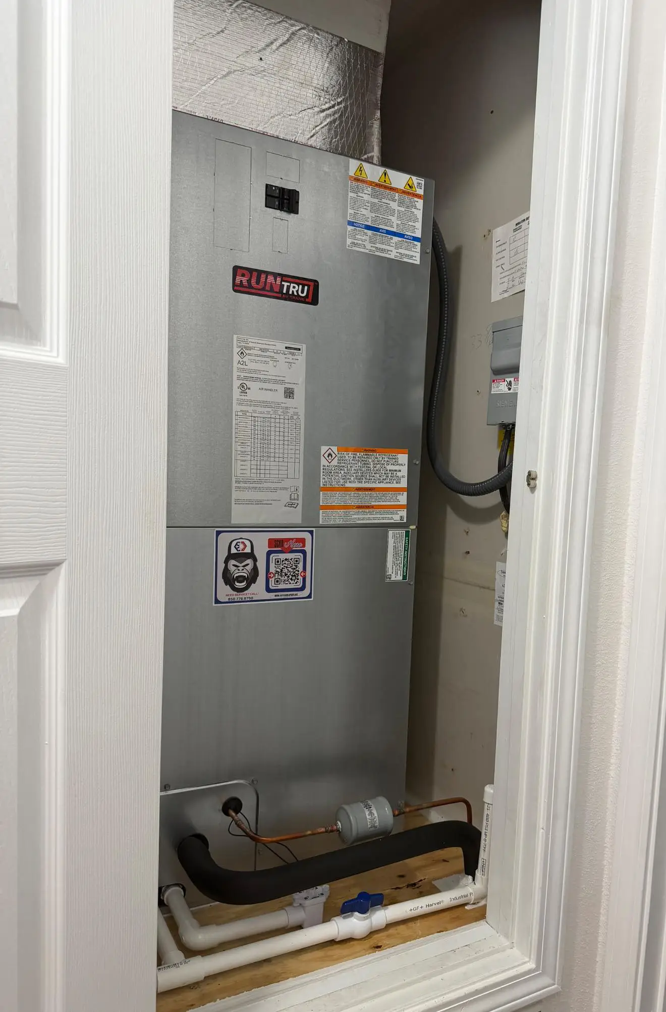 HVAC air handler labeled RUNTRU inside closet with insulated refrigerant lines and PVC condensate drain