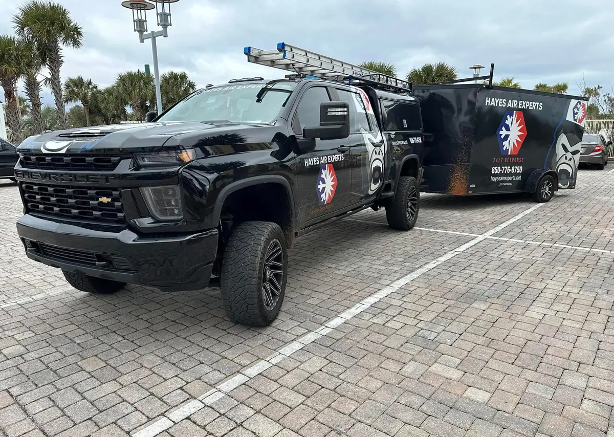 Black Hayes Air Experts service pickup truck with matching trailer parked on a paved brick lot near palm trees