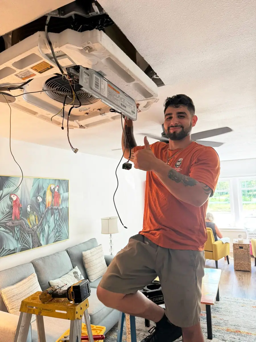 A man giving thumbs up while installing a ceiling air conditioning unit in a living room