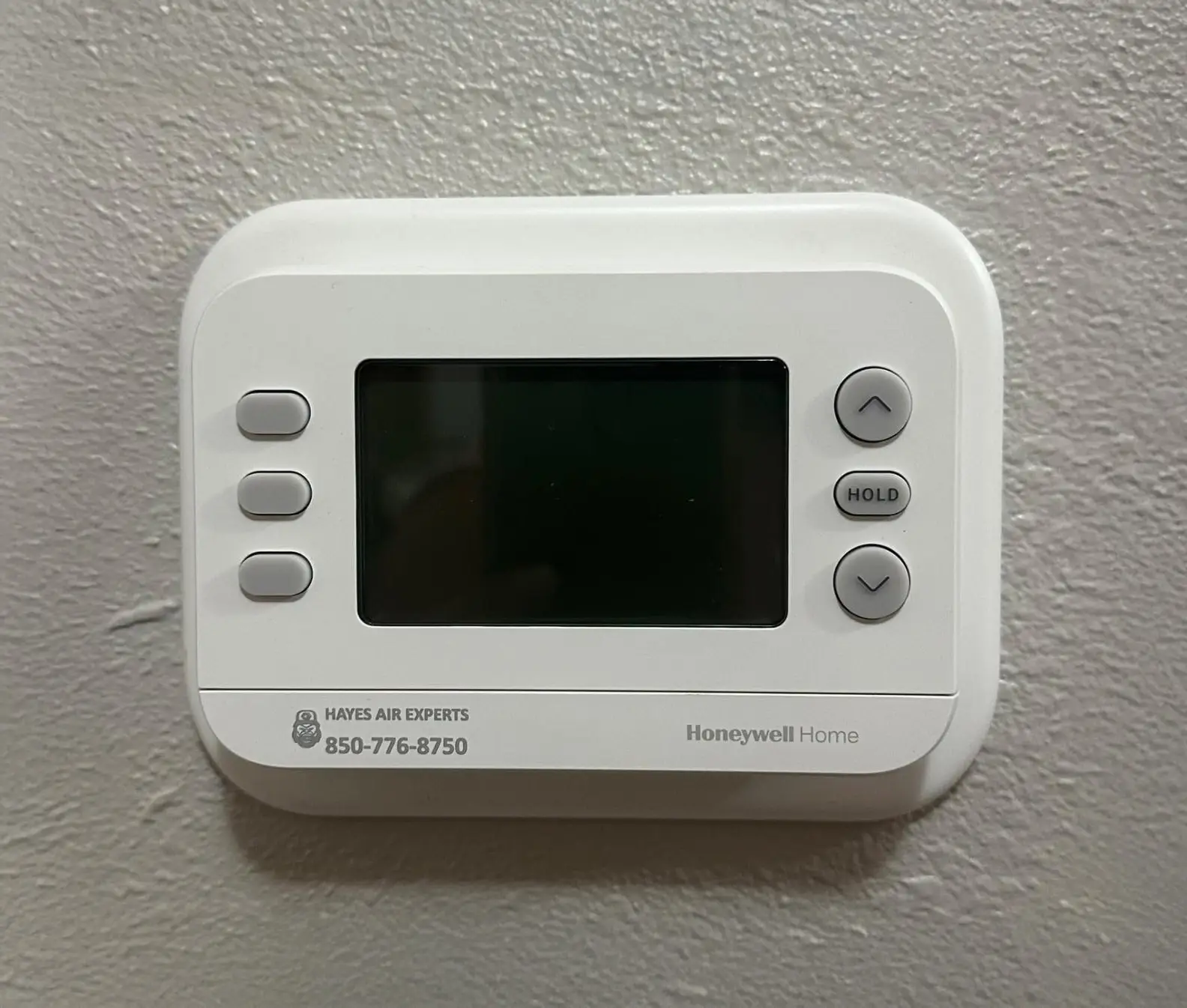 White Honeywell Home digital thermostat with blank screen and up/down buttons mounted on textured wall
