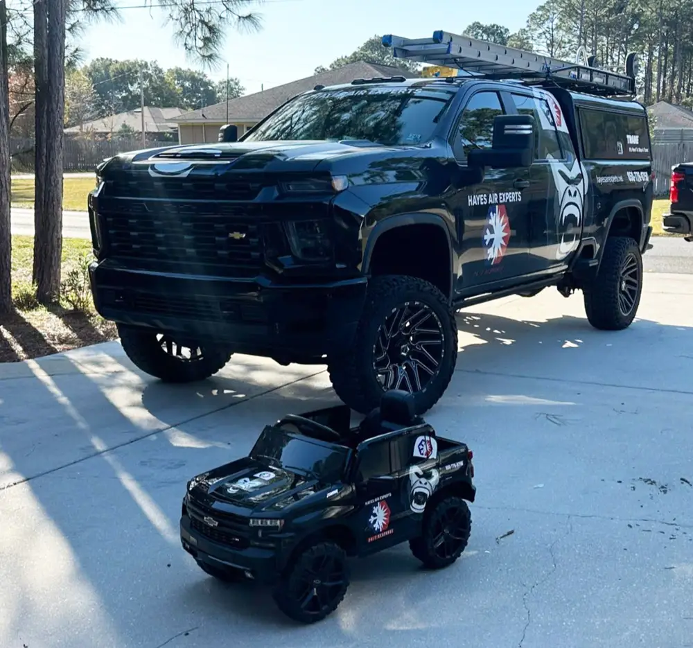 Black Hayes Air Experts work truck with company logo and matching miniature toy truck parked on a residential driveway